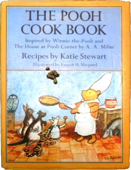 Book cover: Pooh Cook Book. Pooh looks up in the air to follow the trajectory of the turd he is tossing with his frying pan.